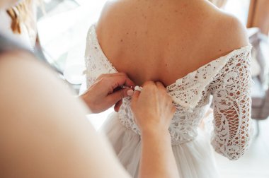 Bir nedime gelinin korselerini sıkıca bağlamasına ve gelinliğini giymesine yardım eder. Düğün sabahına hazırlık konsepti..