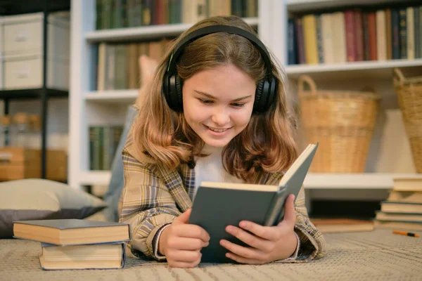 Kız kanepeye oturur ve yanında bir kitap, bir tablet ve kulaklık okur. modern genç evde. gençlik edebiyatı.