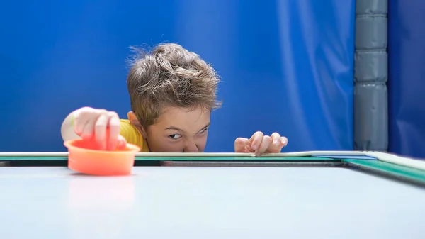 Pojke intensivt och entusiastiskt spela bordshockey.. Ett barn som har vunnit sin air hockey match, med en röd klubba i handen. — Stockfoto