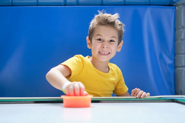 Pojke intensivt och entusiastiskt spela bordshockey.. Ett barn som har vunnit sin air hockey match, med en röd klubba i handen. — Stockfoto