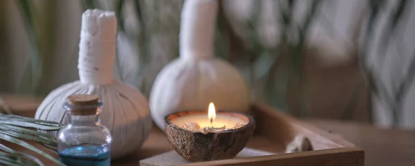 Κερί με άρωμα καρύδας σε ξύλινο τραπέζι. Όμορφη τροπική ιδέα σπα. Σακουλάκια βαμβακερά με βότανα για μασάζ σε ξύλινο φόντο με πράσινα φύλλα. Σφαίρες κομπρέσες — Φωτογραφία Αρχείου