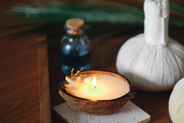 Bougie au parfum de noix de coco sur une table en bois. Beau concept de spa tropical. Pochettes en coton avec des herbes pour massage sur fond de bois avec des feuilles vertes. Boules de compression à base de plantes — Photo