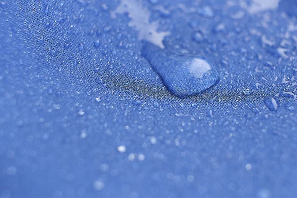 천에 물이 떨어진다. 파란 섬유 방수 섬유 위에 물방울을 비춥니다. 물 은방 수가 되지 않는 천 위에 무늬를 남긴다. 푸른 배경. — 스톡 사진