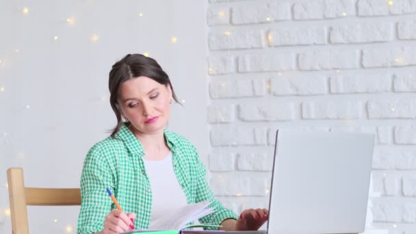 Woman sitting at a table working at a laptop computer. concept of remote work from home. home office in the kitchen. professional freelancer — Stock Video