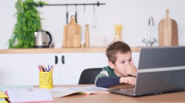Genç bir çocuk dizüstü bilgisayarda oynar ya da internetten ders alır. Asyalı çocuk mutfakta, masada ders çalışıyor.