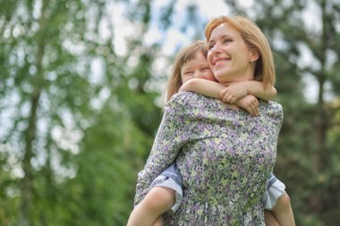 Aile dışarıda eğleniyor. Küçük sevimli kızım annesini sırtında taşıyor. Anne, sevgi dolu çocuğu sırtında taşır ve birlikte eğleniriz..