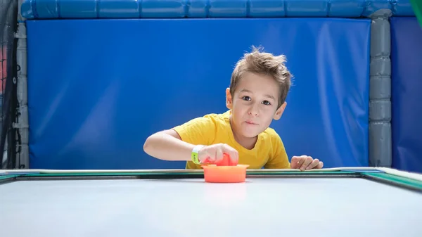 Çocuk dikkatle ve hevesle masa hokeyi oynuyor elinde kırmızı bir çekiçle hava hokeyi maçını kazanmış bir çocuk.. — Stok fotoğraf