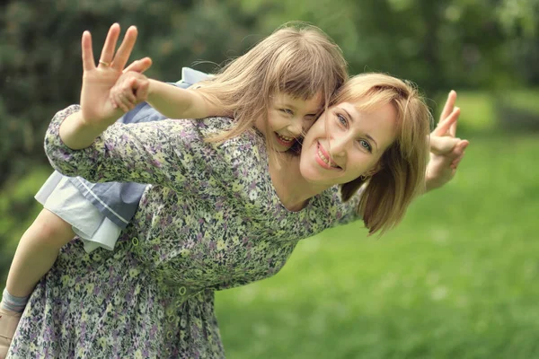 Rodina se baví venku. Malá rozkošná dceruška podpírá svou matku. Máma nosí milující dítě na zádech, směje se a baví se spolu.. — Stock fotografie