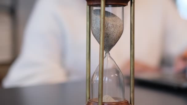 Woman working behind a laptop out of focus, focus on the hourglass. — Stock Video