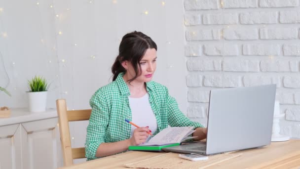 Mulher sentada a uma mesa a trabalhar num computador portátil. conceito de trabalho remoto a partir de casa. escritório em casa na cozinha. freelancer profissional — Vídeo de Stock