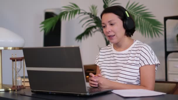 Jovem usa fone de ouvido conferência chamando no laptop conversa com professor on-line estudando, trabalhando em casa . — Vídeo de Stock