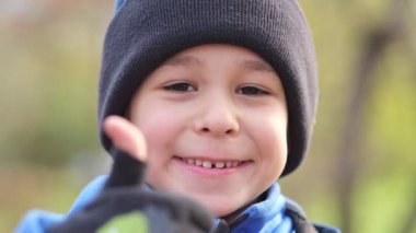 Şapkalı mutlu bir çocuk portresi. Çocuk kameraya başparmak kaldırıyor. Genç çocuk portresi gülümsüyor ve olumlu jest yapıyor.