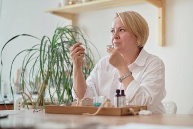 Yağlı ve cam şişeli bir pipetin yakın çekimi. Kadın şişeye parfüm döküyor. Parfüm atölyesi oluşturma