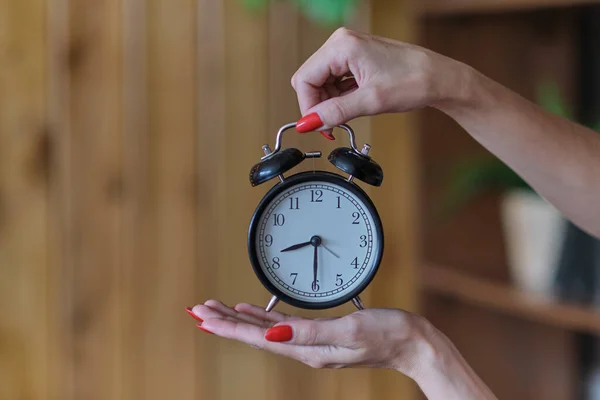 Mãos femininas com manicure vermelho detém um despertador preto. conceito de gestão do tempo — Fotografia de Stock