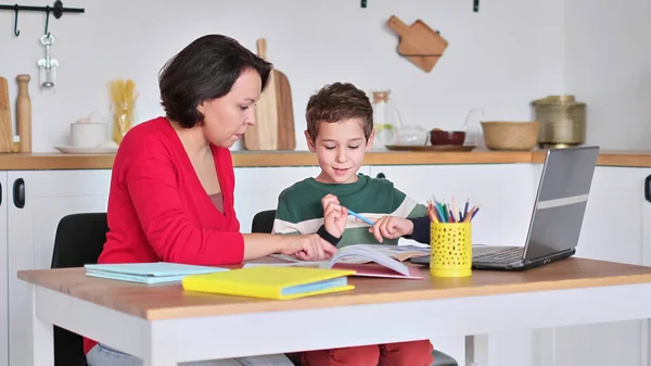 Tutora privada que ayuda a la joven estudiante con la tarea en el escritorio en la sala de niños luminosos. madre ayuda a su hijo a hacer lecciones. educación en casa, lecciones en casa. — Foto de Stock