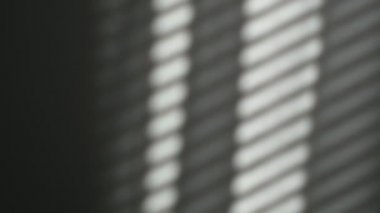 Sabah güneşi odayı aydınlatıyor, arka plan gölgeli. Duvardaki panjurların yansıması, çizgili gölgeler. Rüzgardan perdelerin yavaş hareketi