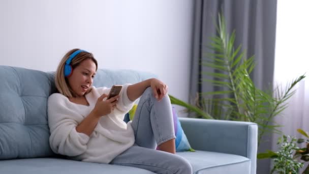 Mulher usando telefone inteligente navegar nas redes sociais, verificar notícias, jogar jogos móveis ou mensagens de texto sentado no sofá. — Vídeo de Stock