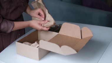 Kadın bir teslimat servisi aracılığıyla bir paket göndermek için kozmetik kavanozlarını bir kutuya koyuyor..