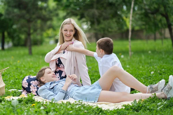 Família passa o fim de semana na natureza. família feliz ao ar livre na grama em um parque. mãe e duas crianças sorrindo. foco suave — Fotografia de Stock