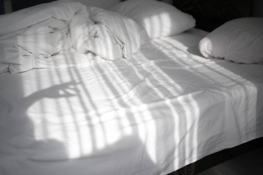 Hafif bir yatak odasındaki bir yatağa güneş ışınları düşer. Rüzgardan hareket eden perdelerin yansıması.