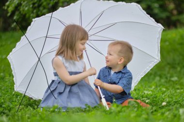 Küçük kız ve oğlan bir şemsiyenin altında saklanıyorlar. Erkek ve kız kardeşler parkta oynuyorlar..