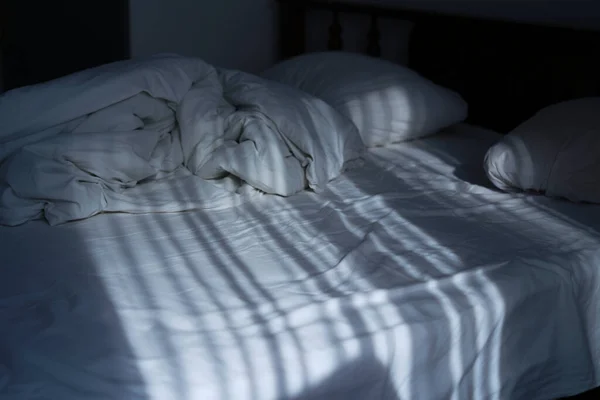 На кровати в светлой спальне лучи солнца падают. отражение штор, движущихся от ветра на смятых постельных принадлежностях — стоковое фото