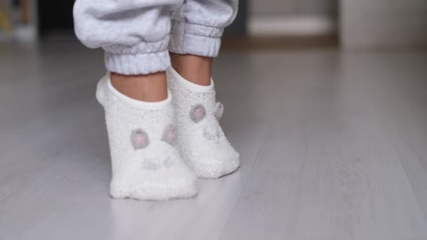 Benen van een vrouw in sokken lopend op de houten vloer van haar huis met een bank op de achtergrond. voeten met witte sokken op grijze houten vloer — Stockvideo