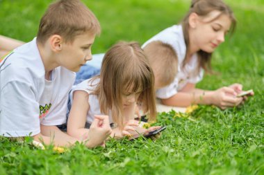 Çimlerin üzerinde cep telefonuyla internet oynayan bir çocuk arkadaş grubu. Mutlu çocuklar çimlerin üzerinde oturan akıllı telefonları kullanıyor. Kardeşlerim..