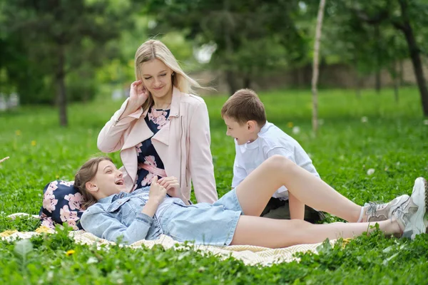 Família passa o fim de semana na natureza. família feliz ao ar livre na grama em um parque. mãe e duas crianças sorrindo. foco suave — Fotografia de Stock