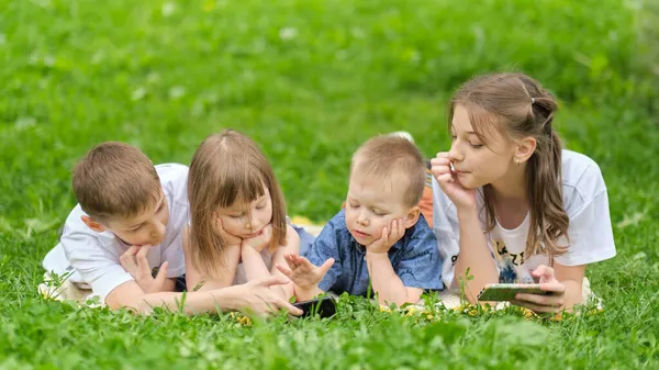 Crianças amigo grupo jogar internet com smartphone móvel na grama. Crianças felizes usando smartphones sentados na grama. Irmãos e irmãs. — Fotografia de Stock