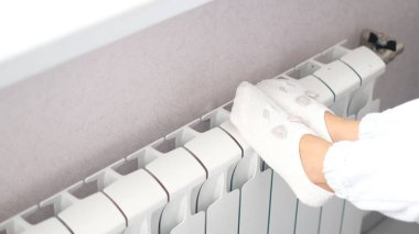 Isınma mevsiminin başlangıcı konsepti. Kadın, soğuk kış zamanı ısıtıcının yanında yün çoraplar örüyor. Kışın evde ısıtıcı kullanmak..