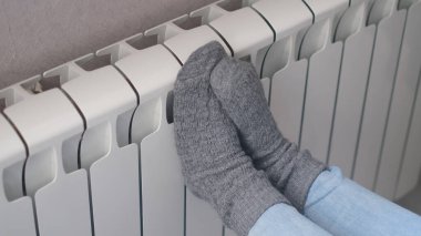 Isınma mevsiminin başlangıcı konsepti. Kadın, soğuk kış zamanı ısıtıcının yanında yün çoraplar örüyor. Kışın evde ısıtıcı kullanmak..