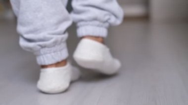Çoraplı bir kadının bacakları arka planda bir kanepeyle evinin ahşap zemininde yürüyordu. Gri ahşap zeminde beyaz çoraplar giyen ayaklar