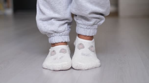 Piernas de una mujer en calcetines caminando sobre el suelo de madera de su casa con un sofá en el fondo. pies con calcetines blancos en piso de madera gris — Vídeo de stock