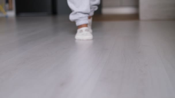Piernas de una mujer en calcetines caminando sobre el suelo de madera de su casa con un sofá en el fondo. pies con calcetines blancos en piso de madera gris — Vídeos de Stock