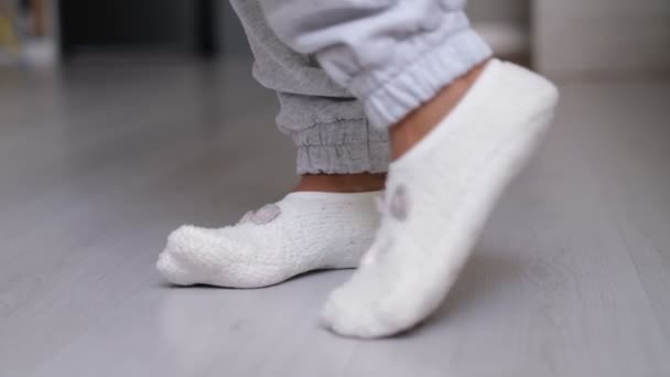 Piernas de una mujer en calcetines caminando sobre el suelo de madera de su casa con un sofá en el fondo. pies con calcetines blancos en piso de madera gris — Vídeo de stock