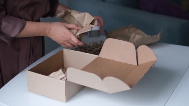 Kvinna packar burkar kosmetika i en låda för att skicka ett paket genom en leverans tjänst. — Stockvideo