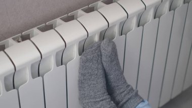 Isınma mevsiminin başlangıcı konsepti. Kadın, soğuk kış zamanı ısıtıcının yanında yün çoraplar örüyor. Kışın evde ısıtıcı kullanmak..