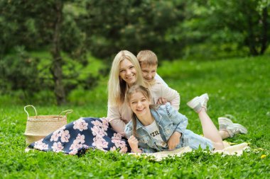 Aile hafta sonunu doğada geçirir. Parktaki çimlerin üzerinde mutlu bir aile. Anne, parkta oynarken, oğlunu ve kızını taşıyor. yumuşak odak