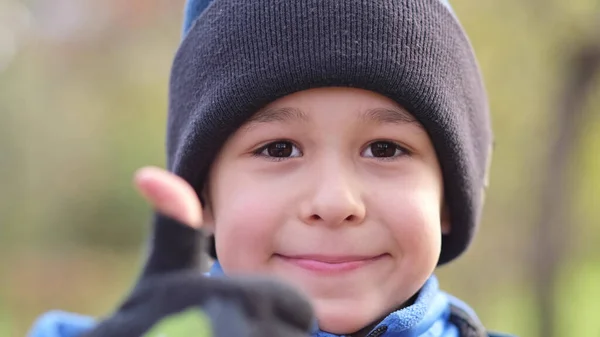 모자를 쓴 어린 소년 이 행복하게 웃는 초상화. 아이들 이 손가락을 카메라에 올리고 있습니다. 어린 소년 이미소짓고 긍정적 인 태도를 취하는 모습 — 스톡 사진