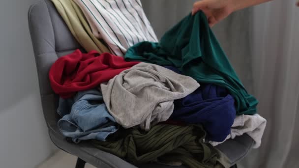 Städerskan tar bort smutsiga kläder från stolen. Blandade klänningar, jeans, kjolar och andra begagnade kläder. Utspädningshem — Stockvideo
