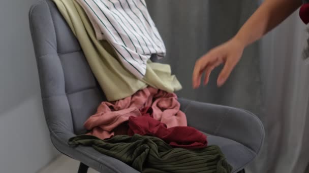 Sprzątaczka zdejmuje brudne ubrania z krzesła. Mieszane sukienki, dżinsy, spódnice i inne używane ubrania. Decluttering do domu — Wideo stockowe