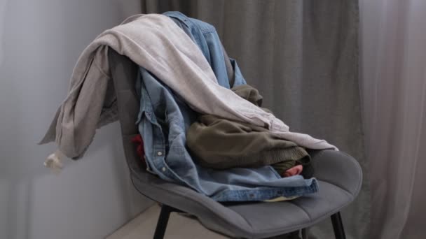 Osoba rzuca używane ubrania na krzesło. Ubrania na krzesło. Kupa zużytych ubrań na datki i recykling. Koncepcja minimalizmu, sprzątania bałaganu i garderoby — Wideo stockowe