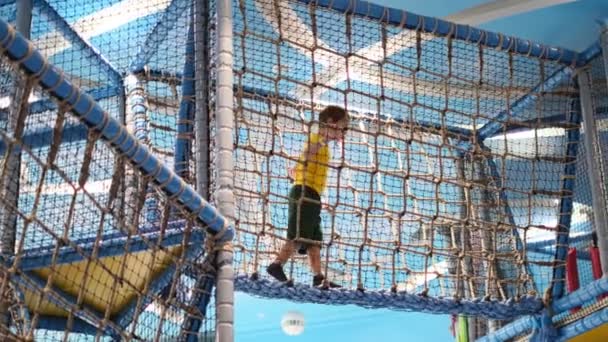 Den lille gutten overvinner en hinderløype på et sportssenter for barn. søt gutt som har det gøy med å leke innendørs i stor skala for barn. – stockvideo