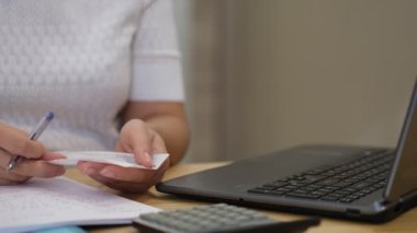 Kadın, aile harcamalarını, hesap makinesini kullanarak, dizüstü bilgisayardan ödeme yapıyor. Faturaları ödeme zamanı. Yoğunlaştırılmış kadın ev giderlerini ödüyor