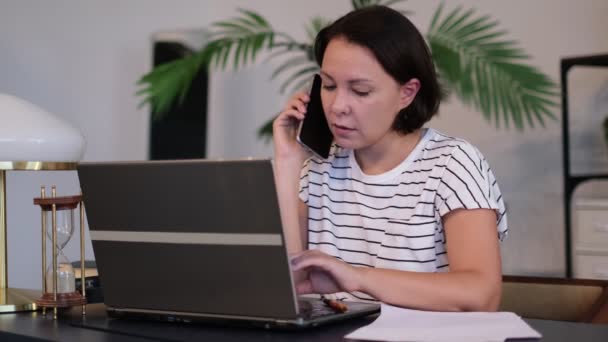 Kvinna ringer sin vän, pratar och frågar om något, använder laptop. frilansare pratar med en kund, eller en anställd förhandlar med en kund — Stockvideo