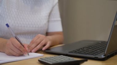 Kadın, aile harcamalarını, hesap makinesini kullanarak, dizüstü bilgisayardan ödeme yapıyor. Faturaları ödeme zamanı. Yoğunlaştırılmış kadın ev giderlerini ödüyor