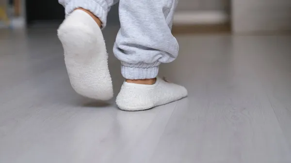 Legs of a woman in white socks walking on the wooden floor of her house with a sofa in the background. feet wearing white socks on gray wooden floor — Stock Photo, Image