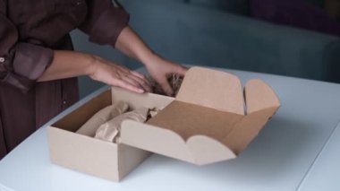 Kadın bir teslimat servisi aracılığıyla bir paket göndermek için kozmetik kavanozlarını bir kutuya koyuyor..