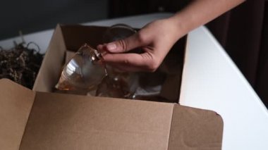 Kadın dükkandan bir teslimat kutusunu açıyor ve kırık bir cam buluyor. Teslimat sırasında paketlenmemiş bir eşya çöktü